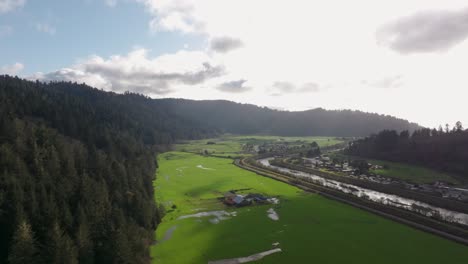 Distant-drone-aerial-view-of-Orick,-California-with-green-fields-and-redwood-forest