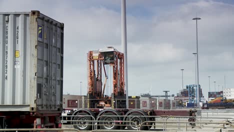 Busy-cargo-terminal-with-a-towering-orange-gantry-crane-handling-shipping-containers,-cloudy-sky-backdrop