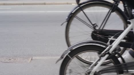 Close-up-of-the-wheels-of-bikes-and-cars-driving-by-in-Copenhagen,-Nørrebro