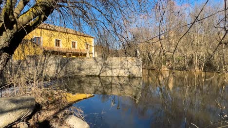 filming-of-the-Adaja-river-as-it-passes-through-Avila-capital-on-the-west-side-where-we-see-the-riverside-trees-without-leaves-because-it-is-winter-and-a-stone-and-yellow-rural-house-in-Spain