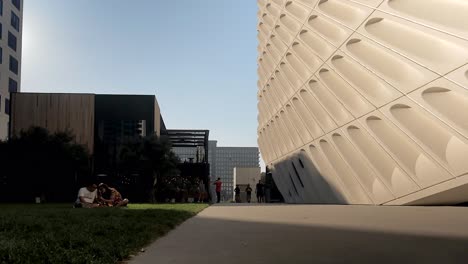 People-walking-next-to-a-little-grass-picnic-area-and-a-beautiful-building