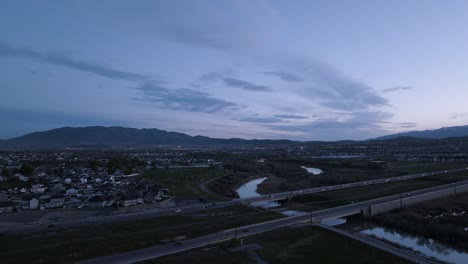 Carretera-Que-Cruza-Un-Río-En-Un-Valle-Debajo-De-Las-Montañas-Al-Atardecer---Revelación-Aérea-De-Retroceso