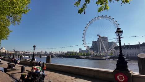 Sunny-day-at-Westminster-Embankment-with-views-of-the-London-Eye-and-River-Thames,-people-enjoying-outdoors