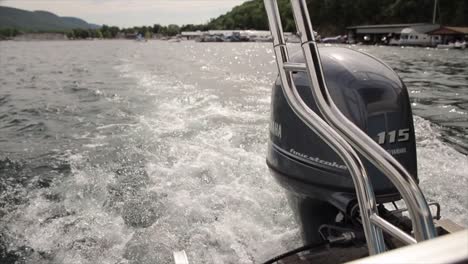 View-of-an-Outboard-Engine-on-a-Pontoon-Motor-Boat-Causing-Through-the-Water-on-a-Lake-with-a-Marina-in-the-Background