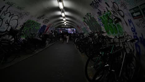 Asian-man-wearing-mask-passing-by-dim,-dark-tunnel-with-graffiti-writing-and-parked-bicycles-in-Shibuya