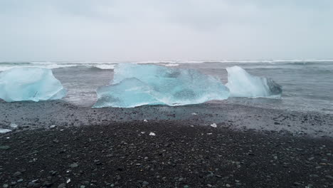 Riesige-Große-Eisblöcke-Am-Schwarzen-Sandstrand-Und-Wellen,-Die-Vom-Meer-Her-Aufschlagen