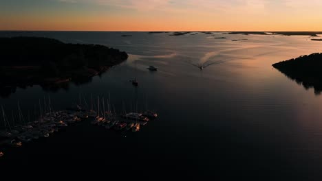 Motorboat-arriving-to-the-Jussaro-marina,-summer-sunset-in-Finland---Aerial-view