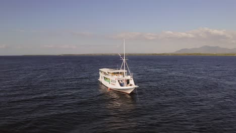 Barco-Turístico-Anclado-Junto-A-Pulau-Bedil,-Una-Pequeña-Y-Hermosa-Isla-Indonesia-Frente-Al-Escudo-De-Lombok,-Vista-Aérea