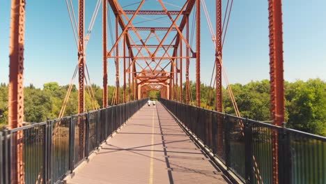 Un-Hombre-Y-Una-Mujer-Caminando-Y-Trotando-En-El-Puente-De-Fair-Oaks-Sobre-El-Río-Americano-En-California---Vista-Aérea-De-Drones-Volando-A-Través-Del-Puente