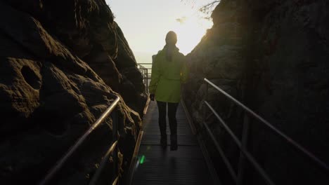 Outdoor-girl-in-yellow-Jacket-walks-on-bridge-against-the-sun,-gimbal-shot