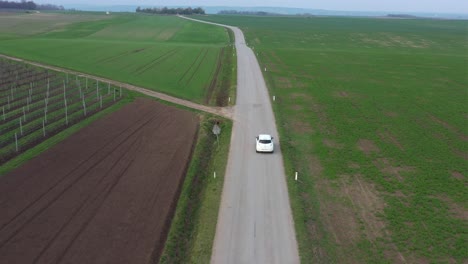 Lonely-white-car-driving-away-on-country-road-through-Lower-Austria,-aerial-view-from-drone-flight