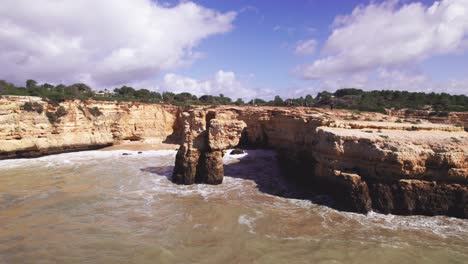 Coastline-view-with-beautiful-orange-rugged-cliffs-with-and-natural-wave-carved-arch-with-groups-of-hikers-by-aerial-4k-drone-at-Albandeira-beach-in-the-Algarve-region-of-Portugal