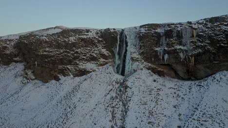 Cascada-De-Seljalandsfoss-Con-Plataforma-Rodante-Aérea-Con-Drones-Para-Revelar-El-Paisaje-Sobre-Acantilados-Cubiertos-De-Nieve,-Islandia