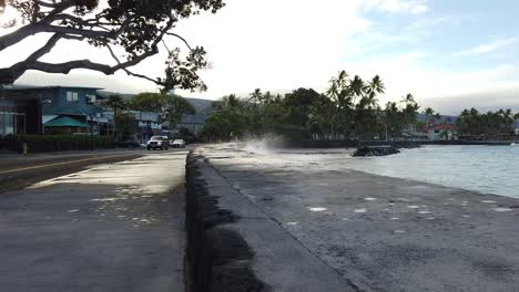 Ola-Salpicando-Contra-Una-Pared-Rompedora-En-La-Playa-Temprano-En-La-Mañana-Mientras-Los-Autos-Pasan-Lentamente