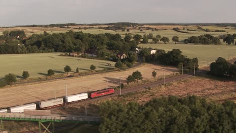 A-freight-train-moving-through-lush-rural-landscape-at-sunset,-aerial-view