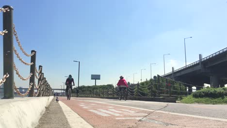 Gente-Andando-En-Bicicleta-A-Lo-Largo-De-La-Orilla-Del-Río,-Yeomchang-dong,-Gangseo-gu,-Seúl,-Corea-Del-Sur