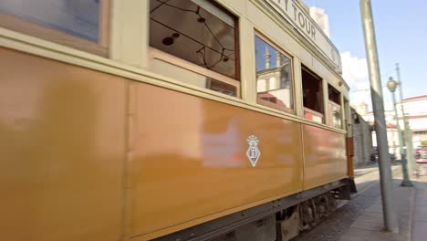 Oldtimer-Straßenbahn-Fährt-Mit-Fußgängern-An-Der-Historischen-Steinkirche-Im-Sonnigen-Porto,-Portugal-Vorbei