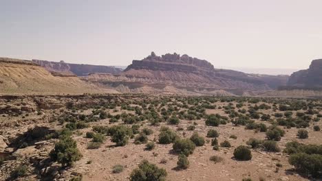 Incredible-beautiful-drone-footage-flying-to-mesa-rock-over-desert-valley,-bushes-and-landscape-in-Black-Dragon-Canyon-in-Green-River,-Utah,-United-States