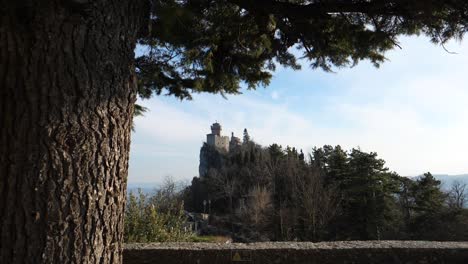 Vista-Deslizante-De-La-Torre-Cesta-En-La-Distancia-En-La-Cima-De-Una-Colina-Llena-De-árboles-En-San-Marino