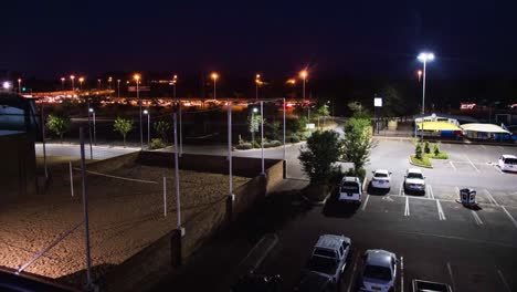 Aparcamiento-Junto-A-La-Cancha-De-Voleibol-Con-Movimiento-Timelapse-De-Coches-Por-La-Noche