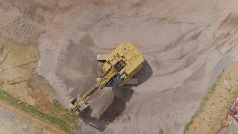 Top-down-aerial-of-a-digger-or-excavator-moving-around-aggrated-or-gravel