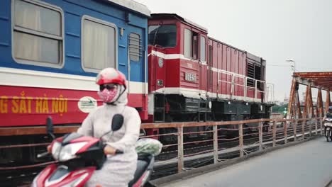 Tren-Que-Pasa-Por-El-Ferrocarril-En-El-Puente-Long-Bien-Con-Gente-Caminando-Por-Un-Carril-Cerca-De-La-Isla-Banana-Tree-En-La-Ciudad-De-Hanoi,-Cau-Long-Bien,-Vietnam