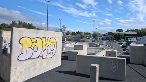 A-boy-practices-pirouettes-on-the-public-skate-park-with-protections-for-blows-to-his-body,-sunny-day,-descriptive-shot