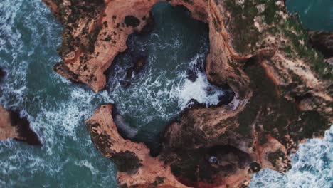 Straight-down-ascending-view-of-eroded-rock-formation-of-coastal-cliffs-and-crashing-waves-by-aerial-4k-drone-at-Ponta-da-Piedade-near-Lagos-in-the-algarve-region-of-Portugal