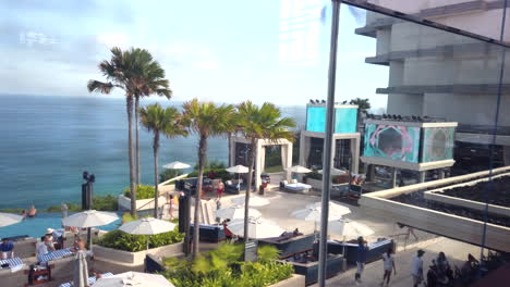 slow-panning-left-behind-glass-windows,-view-of-omnia-beach-club,-impressive-floating-bar-hanging-over-cliff-top