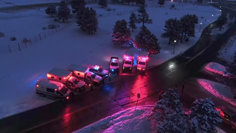 Aerial-orbit-around-emergency-vehicles-with-flashing-lights-at-snowy-intersection