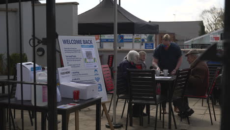 A-pub-beer-garden-entrance-showing-a-waitress-serving-a-table-to-people-sat-outside-after-UK-coronavirus-restrictions-were-eased-on-12-April