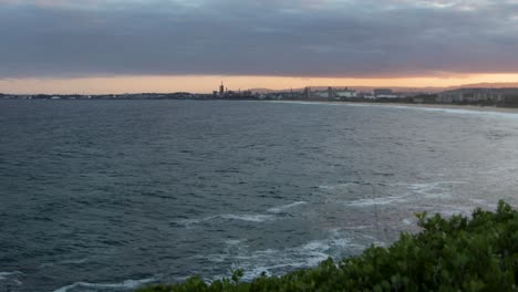 Mar-Ventoso-Durante-La-Puesta-De-Sol-Con-Un-Paisaje-Industrial-Distante-En-Wollongong,-Nueva-Gales-Del-Sur