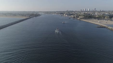 Aerial-pull-away-shot-of-a-white-boat-heading-into-the-Newport-Bay-revealing-Newport-Beach-and-Corona-Del-Mar,-California