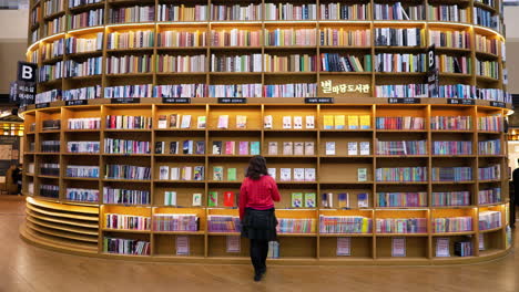 Reisende-Frau-Geht-Auf-Ein-Vom-Boden-Bis-Zur-Decke-Reichendes-Bücherregal-In-Der-Starfield-Library-Coex-Mall-In-Seoul,-Südkorea-Zu