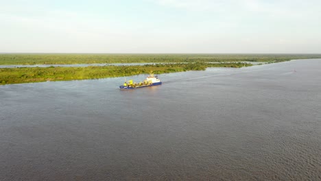 Aproximación-Aérea-Hacia-Adelante-De-Un-Barco-Comercial-Que-Navega-Desde-El-Puerto-De-Barranquilla-En-El-Río-Magdalena-Durante-La-Puesta-De-Sol-De-La-Hora-Dorada.