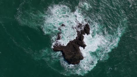 Static-aerial-drone-shot-looking-down-at-large-waves-hitting-a-rocky-island