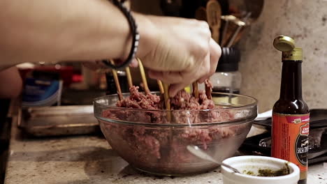 Las-Manos-De-Una-Mujer-Caucásica-Mezclan-Carne-De-Hamburguesa-Cruda-Molida-Con-Tenedores-De-Madera-En-Un-Recipiente-De-Vidrio,-Vista-Lateral-De-Cerca