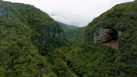 Wunderschöner-Canyon-In-Den-Bergen,-Umgeben-Von-Bäumen,-Mit-Felsigen-Klippen-Und-Einer-Riesigen-Höhle-In-Den-Felsen,-Gefilmt-Von-Einer-Drohne