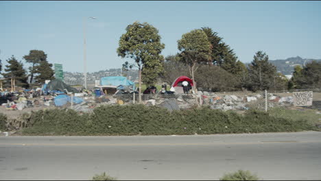 Panning-wide-shot-of-a-homeless-camp-site-next-to-the-freeway-in-Berkeley,-California