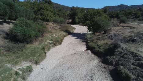 Drone-flight-above-a-dry-riverbed-set-in-a-green-forest-in-greece