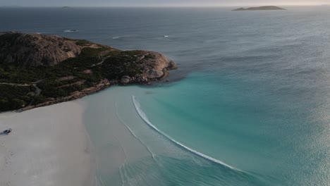 Antena-Arriba-Hacia-Abajo-De-Una-Playa-De-Arena-Vacía-Con-Aguas-Turquesas-De-La-Bahía-Durante-La-Puesta-De-Sol