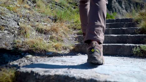 Slow-motion-follow-bottom-half-of-man-walking-up-stone-steps-in-hiking-boots-on-sunny-day