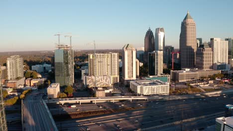 Antena-Del-Tráfico-En-Movimiento-De-La-Autopista-Del-Centro-De-Atlanta,-Construcción-Y-Desarrollo-De-Bienes-Raíces,-Edificios-Del-Horizonte,-Condominios-De-Lujo-Al-Atardecer