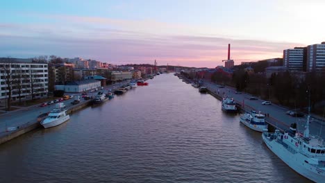 Aéreo,-En-Aumento,-Disparo-De-Un-Dron-Sobre-El-Río-Aurajoki,-Con-Vistas-A-Los-Barcos-Y-La-Ciudad-De-Turku,-Durante-La-Puesta-De-Sol,-En-Varsinais-suomi,-Finlandia