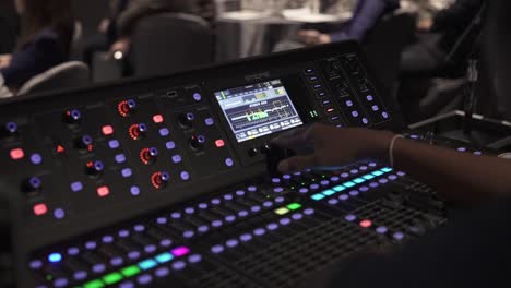 Audio-engineer-adjusting-levels-on-a-sophisticated-mixing-console-at-a-live-event,-low-light