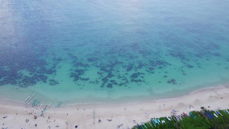 drone-footage-starting-on-Lanikai-Beach-on-the-island-of-Oahu-starting-at-the-white-sand-beach-with-outrigger-canoes-and-heading-out-the-the-blue-green-water-with-coral-reefs