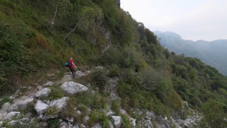 Male-hiker-wearing-backpack-climbs-down-rocky-trail-or-mountain-path,-rear-view