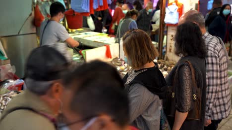 Female-customer-with-mask-buying-perishable-seafood-from-street-vendor-at-a-local-marketplace,-static-shot