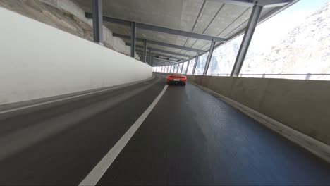 Ferrari-En-Los-Alpes-Conduciendo-Rápido-A-Lo-Largo-De-Un-Túnel-De-Paso-De-Montaña-Visto-Con-Un-Disparo-De-Drone-Desde-Fuera-Del-Túnel-Justo-Al-Lado-Del-Automóvil