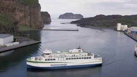 Ferry-boat-entering-harbor-of-Vestmannaeyjar-makes-turn-to-dock,-lowering-aerial